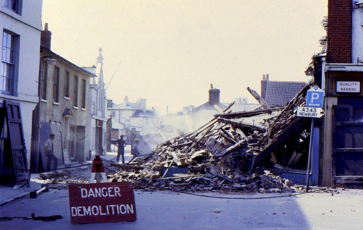 Start of demolition of shops and buildings on West Street. The shops behind the Guildhall would be next.  Today the site of the Chantry Centre entrance.  The High Street took two way traffic to and from Bridge Street and is evidence by the direction sign 